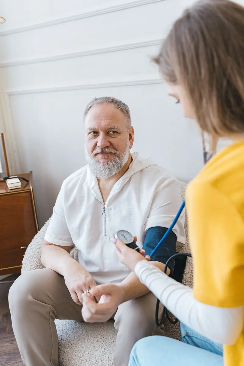 Verpleegkundige meet bloeddruk bij oudere man thuis (tijdelijke stockfoto, Pexels 7345476)